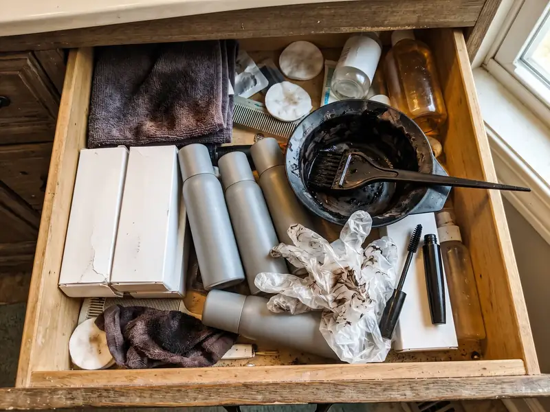 A bathroom drawer full of half-used hair color products, sprays and gloves
